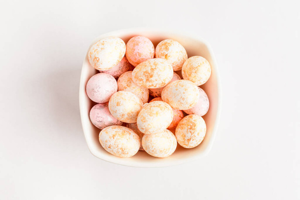 Pink chocolate coated Easter eggs candies on a bowl isolated on a white table, tasty sugary dessert for children - Фото, изображение