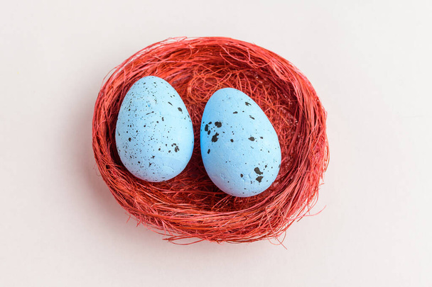 Два синього кольору декоративні великодні яйця в червоному сільському кошику ізольовані на білому столі
 - Фото, зображення