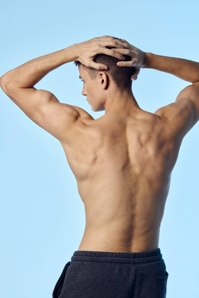 atleta culturista sostiene sus brazos detrás de su espalda bombea los músculos del brazo vista posterior - Foto, Imagen