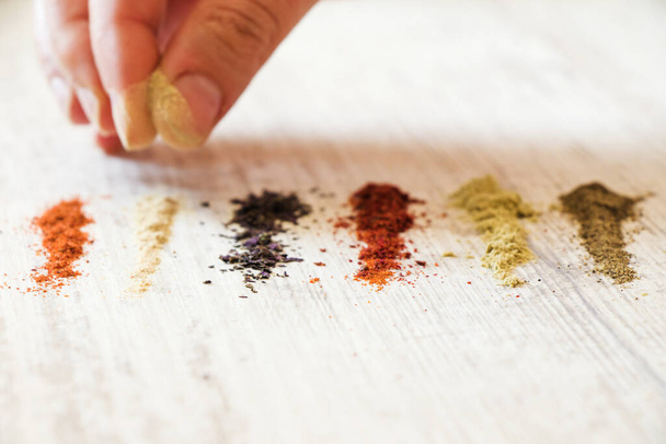 A closeup shot of a person putting different colorful spices on the white wooden table with his hand - Fotoğraf, Görsel