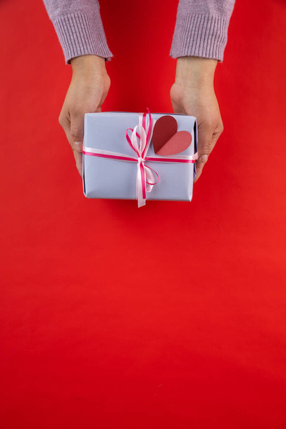 A vertical shot of female hands holding red gift box isolated on red background - Foto, Bild