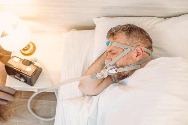 L'homme endormi avec des problèmes respiratoires chroniques envisage d'utiliser la machine CPAP au lit. Soins de santé, Apnée du sommeil obstructive, CPAP, concept de ronflement - Photo, image