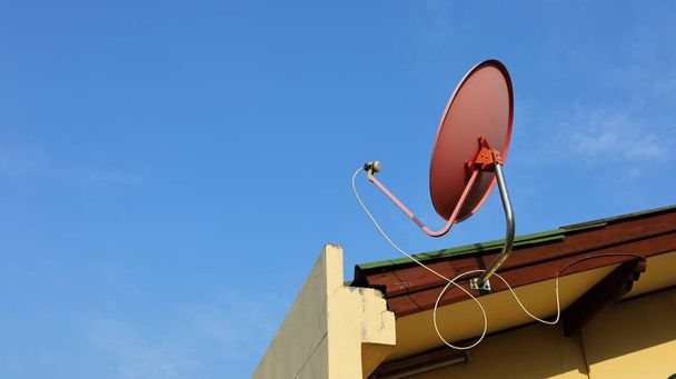 Satellitenschüssel auf dem Dach. Rote Metallschüssel und TV-Receiver steuern Nachrichten mit Satellitentechnik auf einem hellen Himmelshintergrund mit Kopierraum an. Inhalte und Schwerpunkte wählen - Foto, Bild