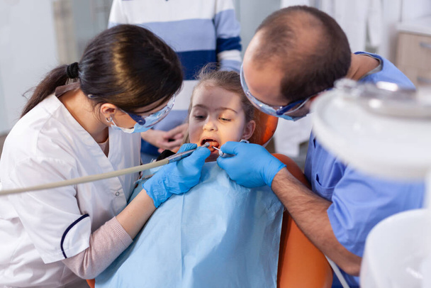 Dentista y asistente usando instrumentos durante el tratamiento dental para niña - Foto, Imagen