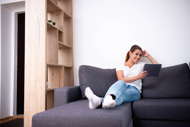 Bella donna che usa il suo tablet su un divano in soggiorno - Foto, immagini