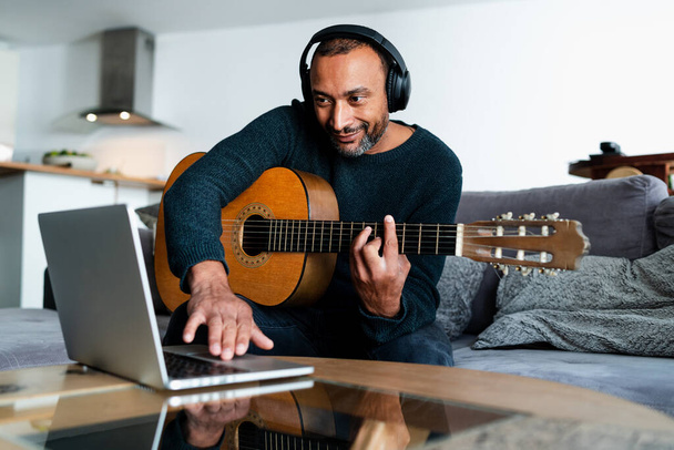 Entspannter Mann spielt zu Hause Gitarre und benutzt Laptop - Foto, Bild