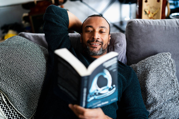 40 років чоловік розслабляється на дивані і читає книгу
 - Фото, зображення