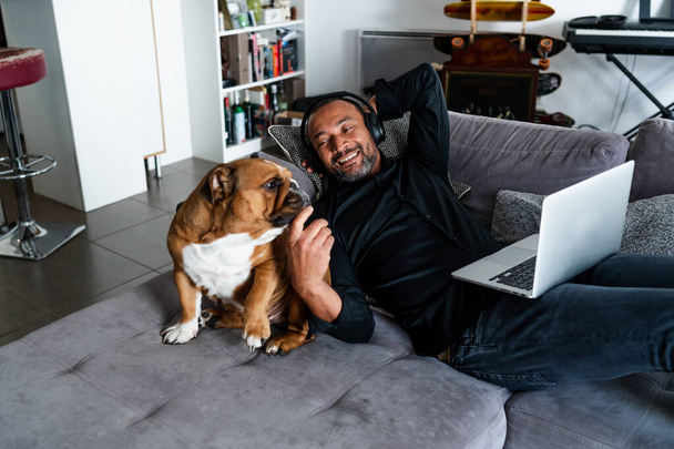 Middle aged man relaxing on the sofa and watching a movie next to his dog - Photo, Image