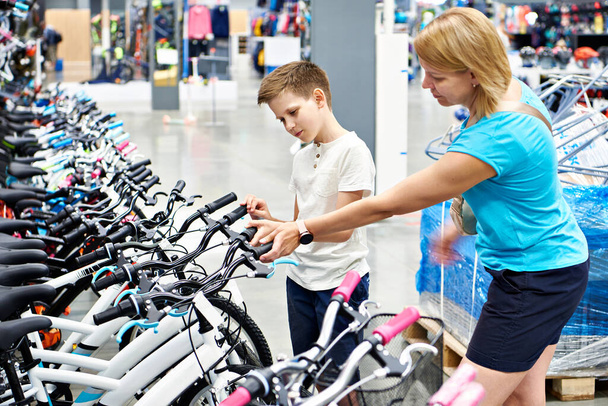 Boy and mother choose  bicycle in sporting goods store - Photo, Image