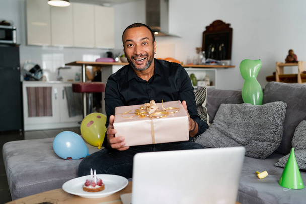Viruspandemia ja sosiaaliset vaikutukset: 40-vuotias mies juhlii syntymäpäiväänsä kotona tietokoneellaan puhuakseen perheensä kanssa - Valokuva, kuva