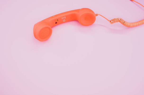A high angle shot of a vintage orange telephone on a pink surface - Fotó, kép