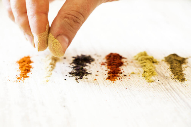 A human putting different colorful spices  on the white wooden table - Фото, зображення