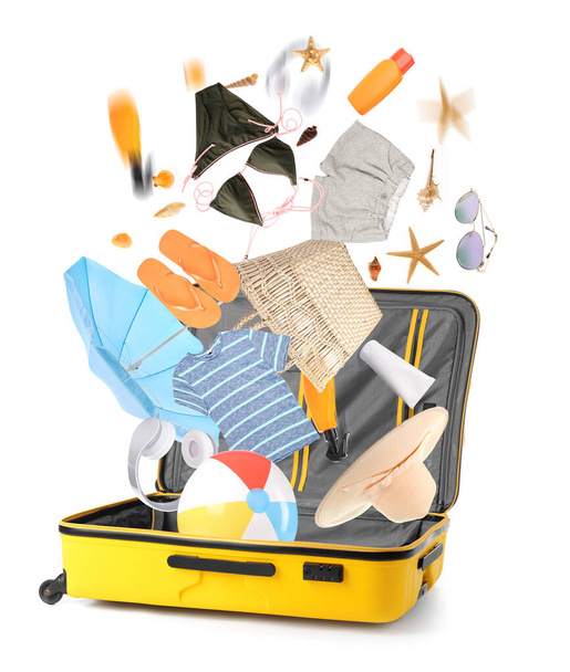 Open suitcase with falling beach accessories on white background - Photo, Image