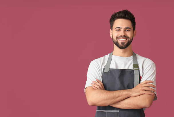Young man wearing apron on color background - Photo, Image