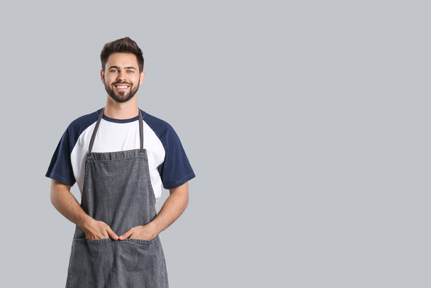 Young man wearing apron on grey background - Foto, Imagen