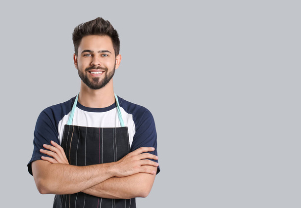 Young man standing wearing apron on grey background - Foto, afbeelding