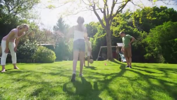 νεαρό κορίτσι που παίζει ποδόσφαιρο με την οικογένειά της σε εξωτερικούς χώρους σε μια ηλιόλουστη ημέρα - Πλάνα, βίντεο
