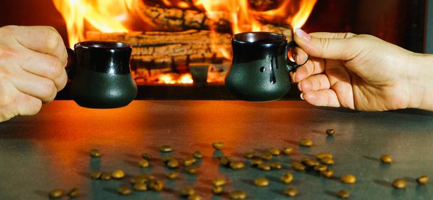 Romantischer Abend. Paar bei einer Tasse Kaffee am Feuer. Nahaufnahme von Händen im Gegenlicht eines brennenden Kamins. - Foto, Bild