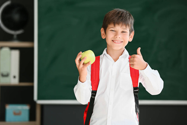 Schoolboy με μήλο σε θολή φόντο στο σχολείο - Φωτογραφία, εικόνα