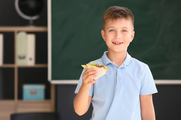 Schoolboy with sandwich against blurred background in school - Photo, image