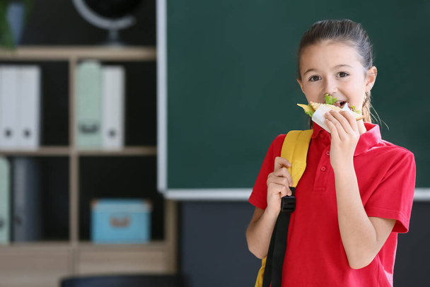 Schulmädchen isst Sandwich vor verschwommenem Hintergrund in der Schule - Foto, Bild