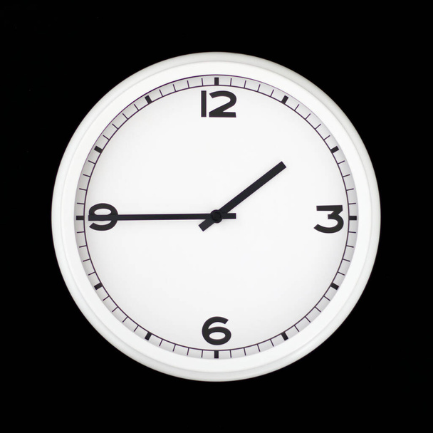 Λευκό στρογγυλό αναλογικό ρολόι τοίχου απομονωμένο σε μαύρο φόντο, δύο παρά τέταρτο. - Φωτογραφία, εικόνα