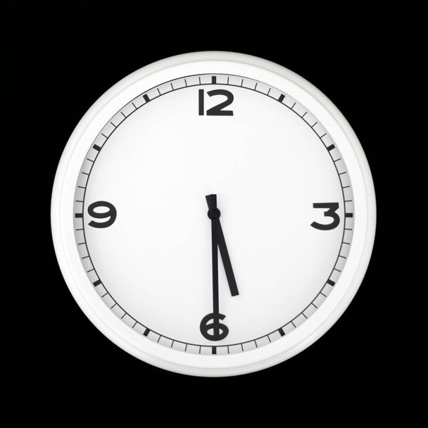 Biały okrągły analogowy zegar ścienny izolowany na czarnym tle, wpół do piątej. - Zdjęcie, obraz
