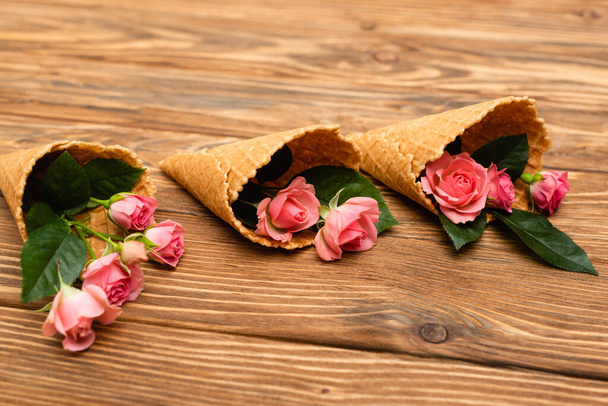 pink tea roses in waffle cones on wooden surface - Fotó, kép
