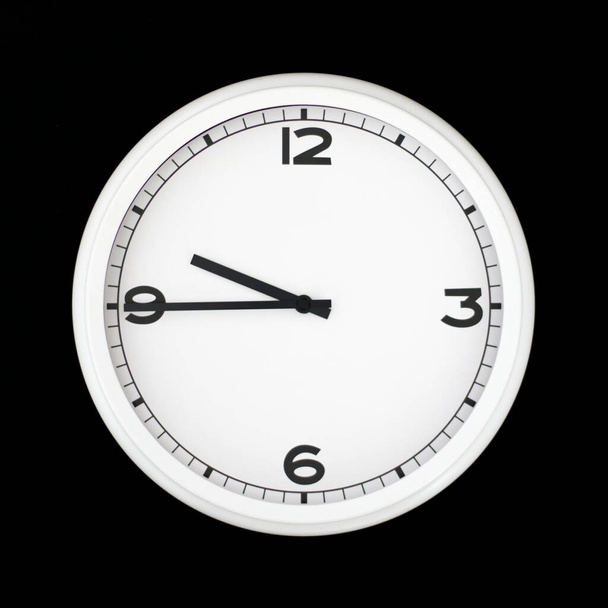 White round analog wall clock isolated on black background, its quarter to ten. - Photo, Image