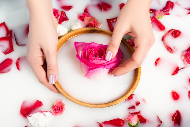 cropped view of woman holding wooden bowl with pink peony near flowers in milky water  - Fotografie, Obrázek