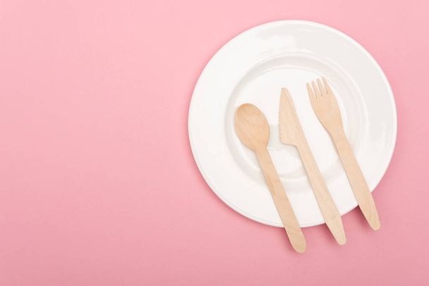 top view of wooden cutlery on white plate isolated on pink  - Photo, Image