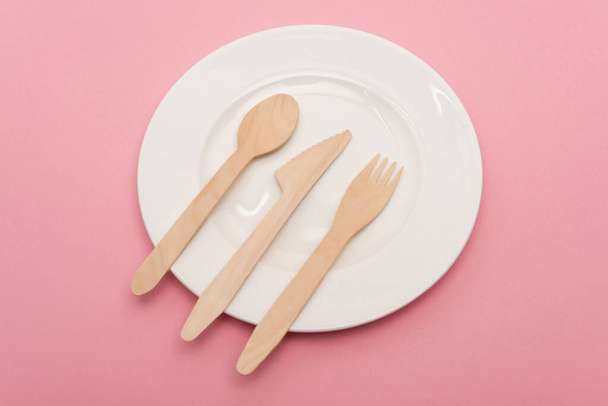 top view of disposable wooden cutlery on white plate isolated on pink  - Foto, immagini