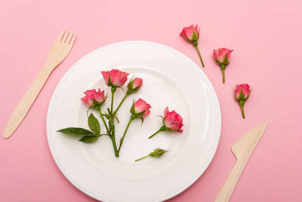 top view of wooden cutlery near white plate with flowers isolated on pink  - Zdjęcie, obraz