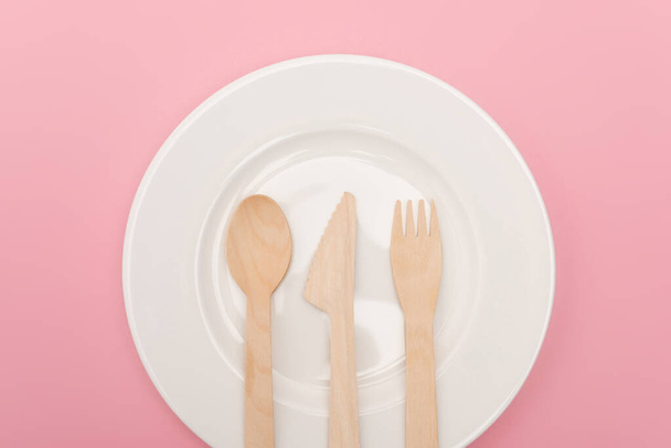top view of disposable wooden cutlery on plate isolated on pink  - Фото, изображение