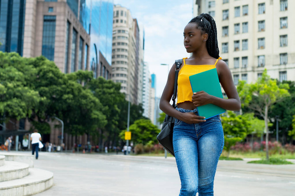 Thinking afro american female student with braids and backpack outdoor in city in summer - Fotoğraf, Görsel