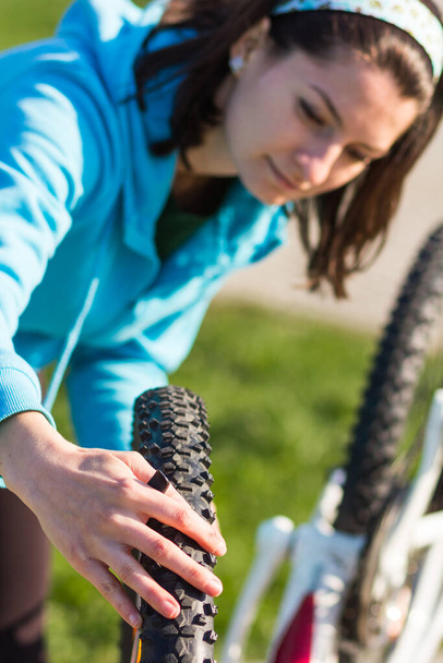 Blurry pose of an active woman checking bike's wheel . Focus on the wheel - 写真・画像