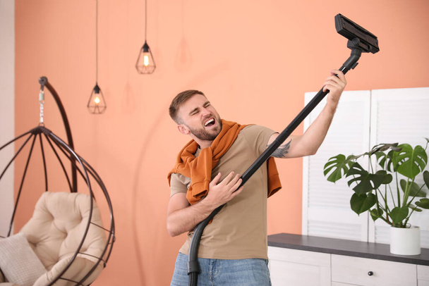 Young man having fun while vacuuming at home - Foto, afbeelding