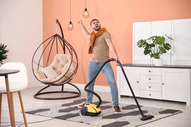 Young man having fun while vacuuming at home - Фото, изображение