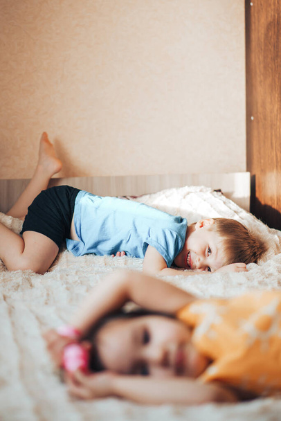 Gyerekek fekszenek az ágyon. Testvérek játszanak az ágyon. Gyereknevelés és gondozás. Koncentrálj a fiúra.. - Fotó, kép