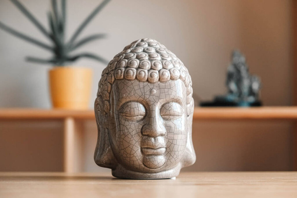 Ceramic statuette of a Buddha head on a wooden shelf. Copy, empty space for text. - Foto, Imagem