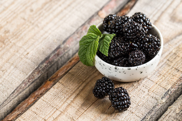 fresh juicy blackberries with green leaves in a plate on a wooden table. healthy berry, antioxidants, antiage foods. - Photo, Image