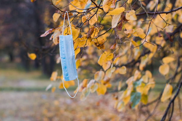 Gesichtsmaske hängt im Herbstpark an einem Baum - Foto, Bild