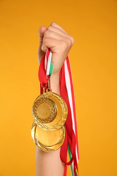Woman holding gold medals on yellow background, closeup - Foto, Imagen
