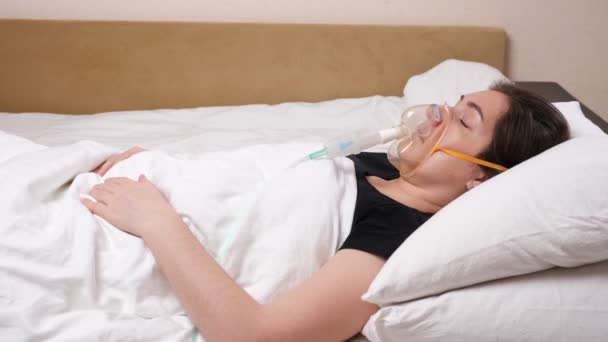 Νεαρή γυναίκα με μια μάσκα στο πρόσωπό της βρίσκεται σε ένα λευκό κρεβάτι - Πλάνα, βίντεο