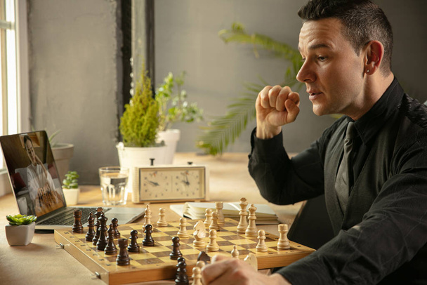 Mladý kavkazský muž šachista hraje šachy online pomocí notebooku. - Fotografie, Obrázek