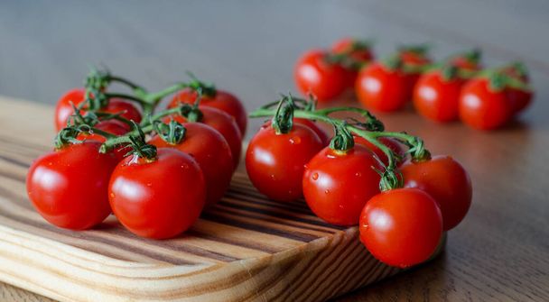 A branch of cherry tomatoes on wooden cutting board. selective focus - Фото, зображення