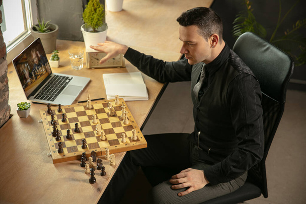 Joven jugador de ajedrez caucásico jugando ajedrez en línea con su estudiante. - Foto, Imagen