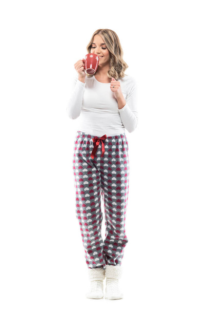 Happy relaxed young woman in pajamas and warm socks holding mug drinking coffee or tea. Full length portrait on white background. - 写真・画像