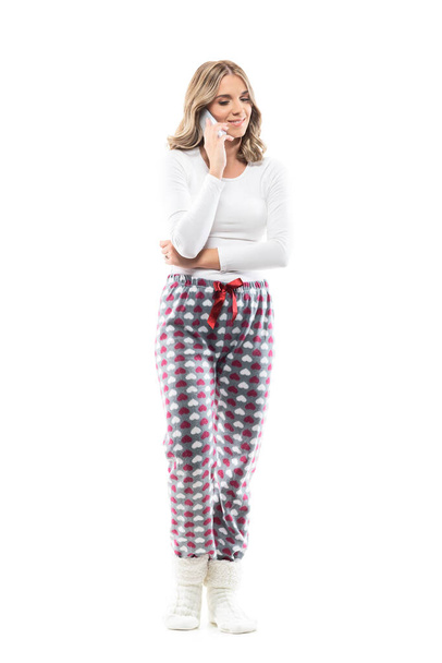 Relaxed young woman in casual sleepwear home clothes talking on the phone looking down. Full length portrait on white background. - Photo, Image