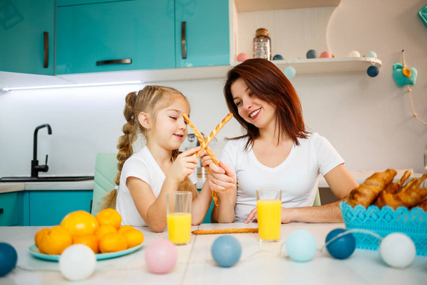 Happy family, mom and daughter are sitting in the kitchen and eating bread sticks. Family relations of the child with the parents - Photo, Image